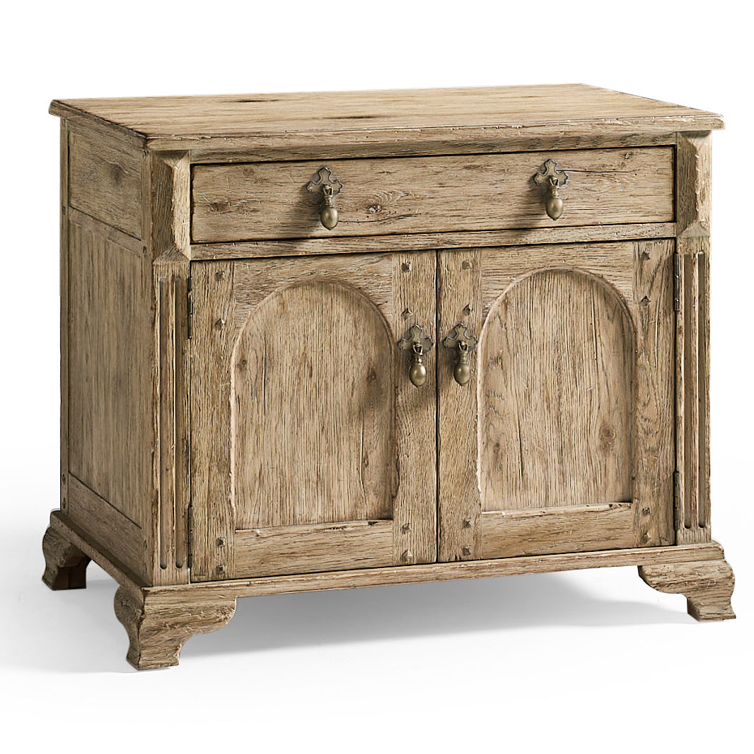 Front view of Sagehill oak bedside table featuring arched panel doors, brass cross-backplate pulls, and distressed grey-brown finish