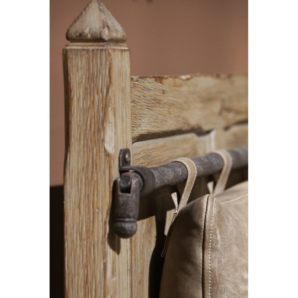 Close-up of weathered oak post with iron rod and beige suede cushion loops on hall bench