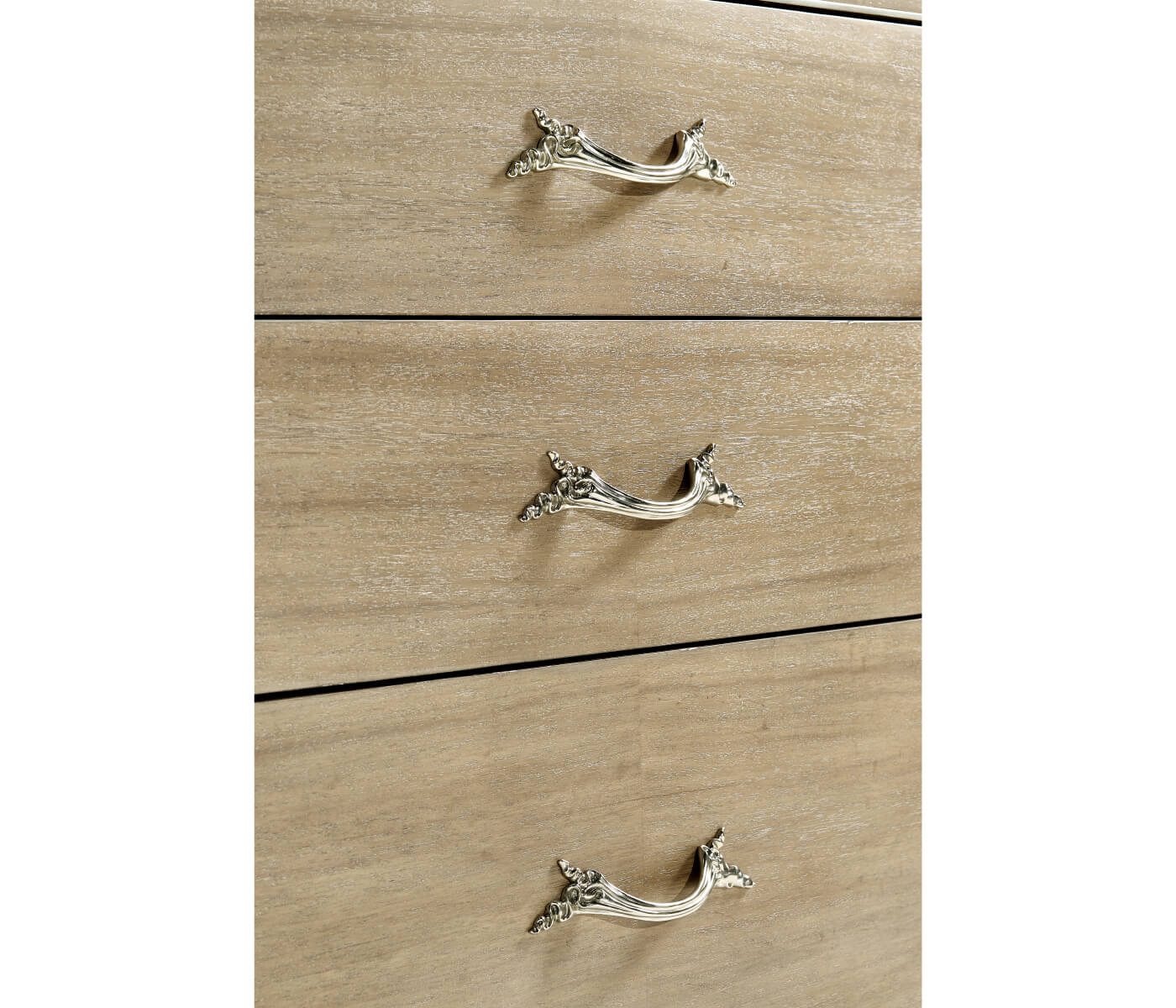 Detail shot of three drawers showing light brown wood grain texture and intricate silver scrollwork leaf handles