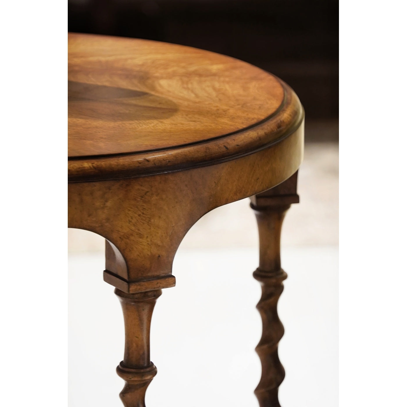 Close-up detail of caramel walnut tabletop edge, arched apron support, and spiral leg junction