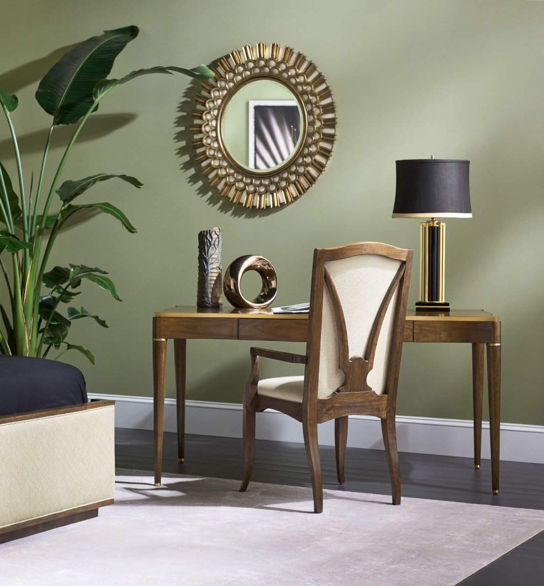 Hollywood Regency style round mirror mounted on sage green wall above wooden desk