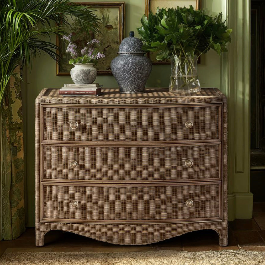 Lifestyle shot of Jonathan Charles rattan bow front chest styled against green wall with decor