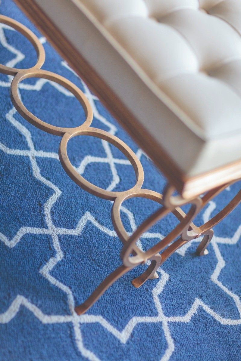 Close-up of Jonathan Charles Bench Circles showing gilded iron interlocking circle base on blue geometric rug